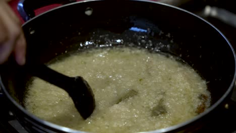 a person is gently twirling a spoon within a pot, carefully stirring onions, embodying the concept of cooking and the preparation of nutritious meals, captured in slow motion