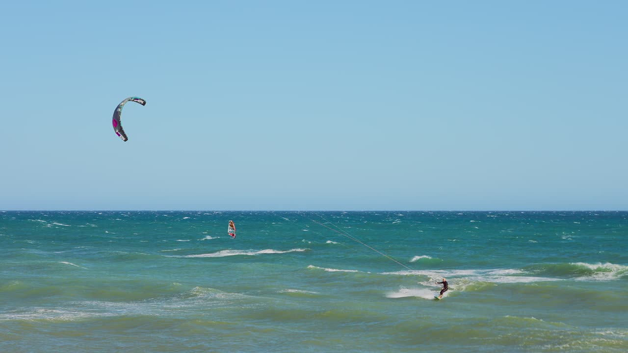 cometas y surfistas de viento en cámara lenta en un día ventoso con un cielo despejado