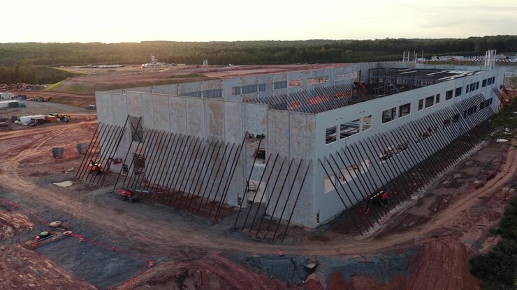 Reihen von Stahlstützen halten die Betonwände eines Rechenzentrums in Louisa County, Virginia, während rot grundierte Dachträger das letzte Licht eines dunstigen Sonnenuntergangs einfangen. Luftaufnahme