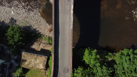 An-old-stone-bridge-with-a-man-walking-in-opposite-direction,-aerial