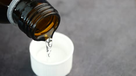 pouring medicine from a brown bottle into a white cap