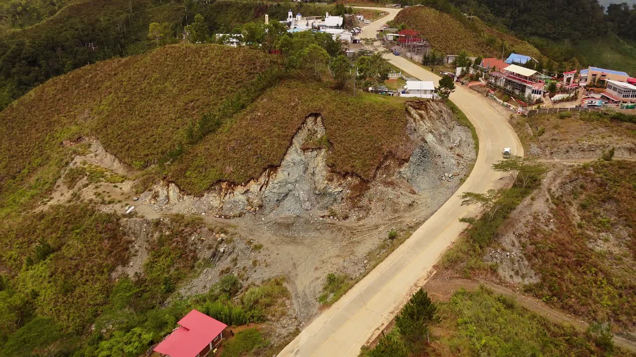 Drone shot of a winding rural road connecting hills to a small remote village. Great for infrastructure, development, and travel or environmental storytelling projects