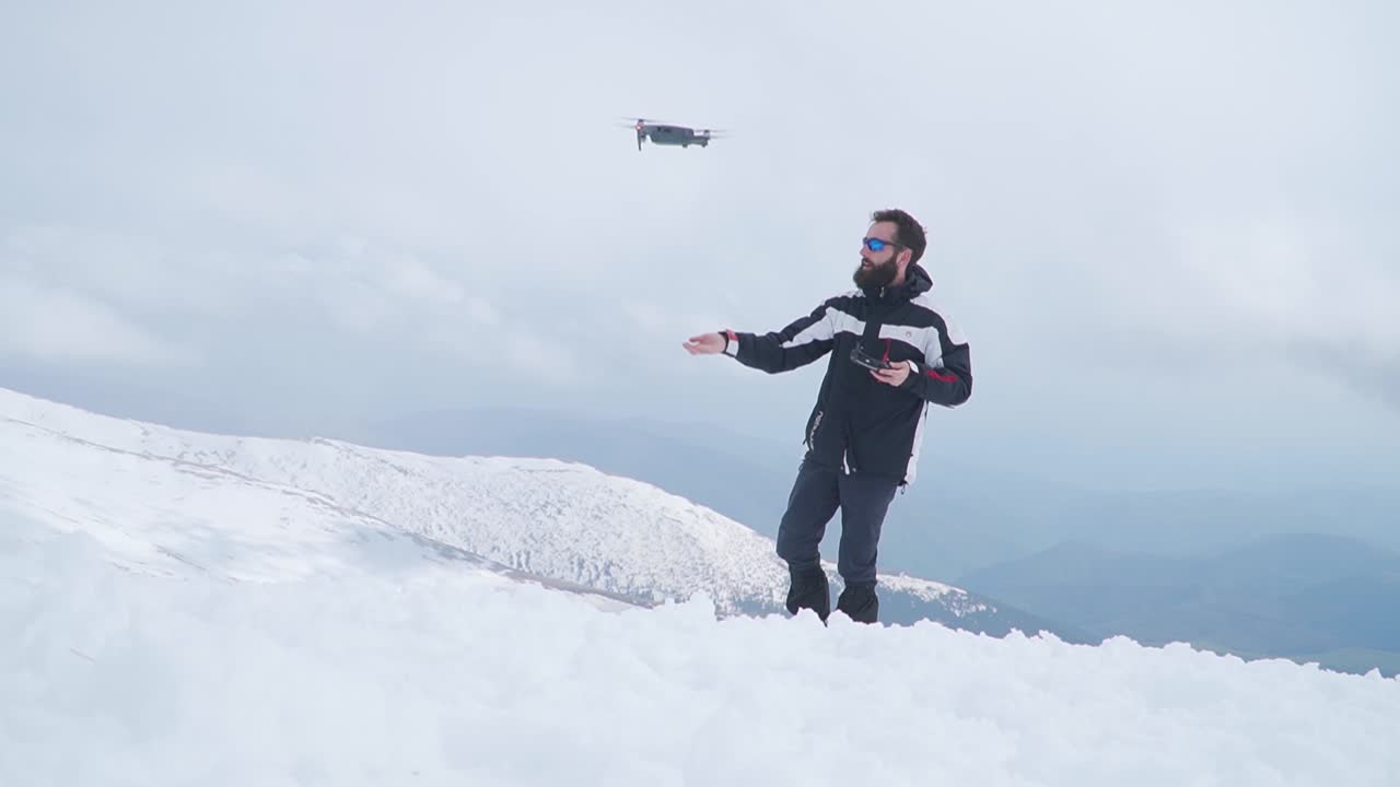 hombre con barba lanza un avión no tripulado de la mano mientras está de pie en la nieve en lo alto de la montaña