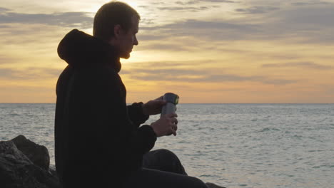 man closes thermos, then leaves during golden hour near sea