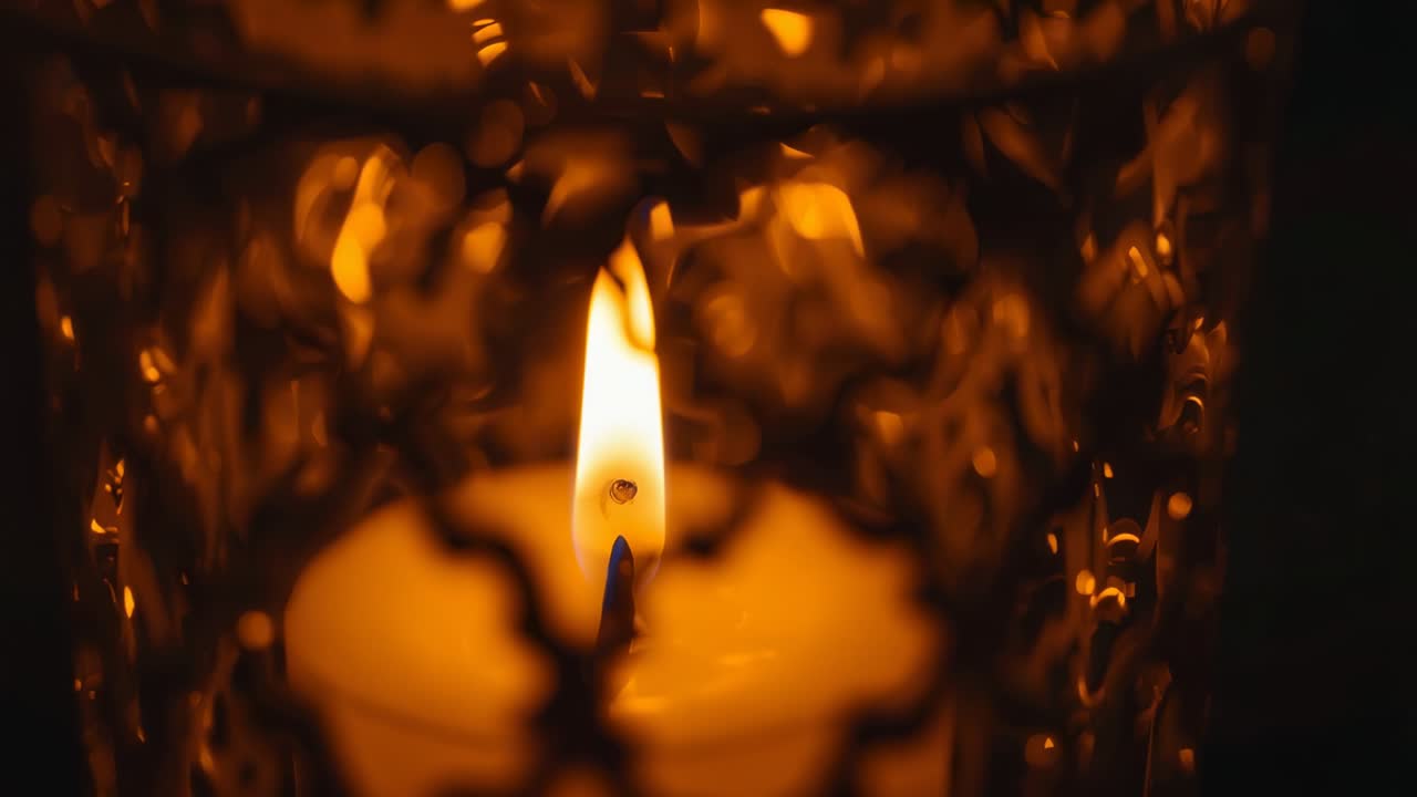 Opening shot showing candle flame flickering inside glass holder in dark room, casting warm glow