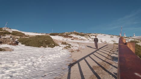 Vista-Frontal-De-Un-Joven-Excursionista-Caminando-Por-Una-Carretera-En-El-Pico-De-Una-Montaña-Nevada-En-El-Parque-Nacional-De-Guadarrama,-Madrid,-España