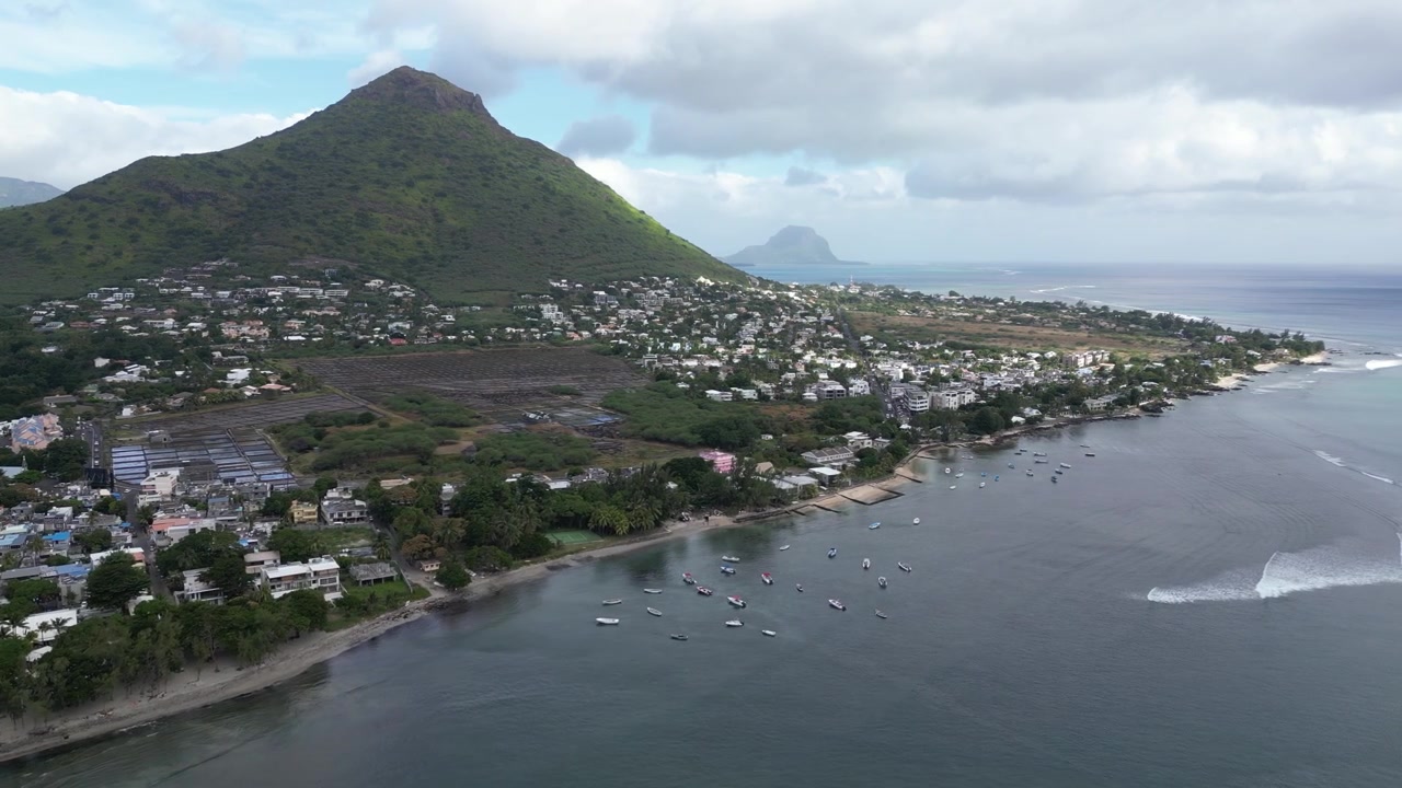 Vista aerea con drone di Tamarin Beach e del villaggio costiero a Mauritius, con l'iconica cima montuosa Trois Mamelles che si erge sullo sfondo. Panorama di una destinazione di viaggio su un'isola tropicale.