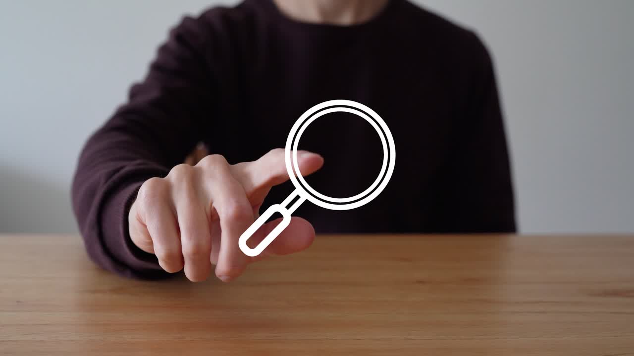 Person In Dark Shirt Sits At Wooden Table, Tapping Magnifying Glass Icon To Make It Vanish. closeup shot