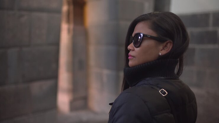 Una donna asiatica, che indossa occhiali da sole, si volta per ammirare l'architettura di Qorikancha a Cusco