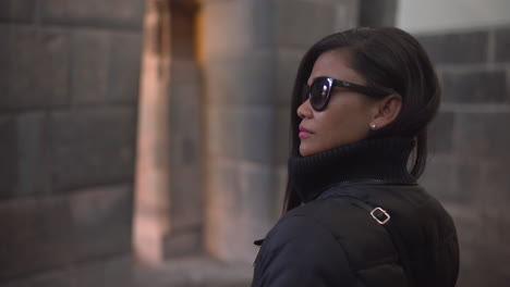 una mujer asiática, con gafas de sol, se da la vuelta para admirar la arquitectura de qorikancha en cusco