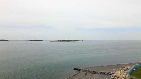 Aerial-pull-back-showing-Wind-Turbine-on-Coast-of-Massachusetts,-showing-football-field-underneath