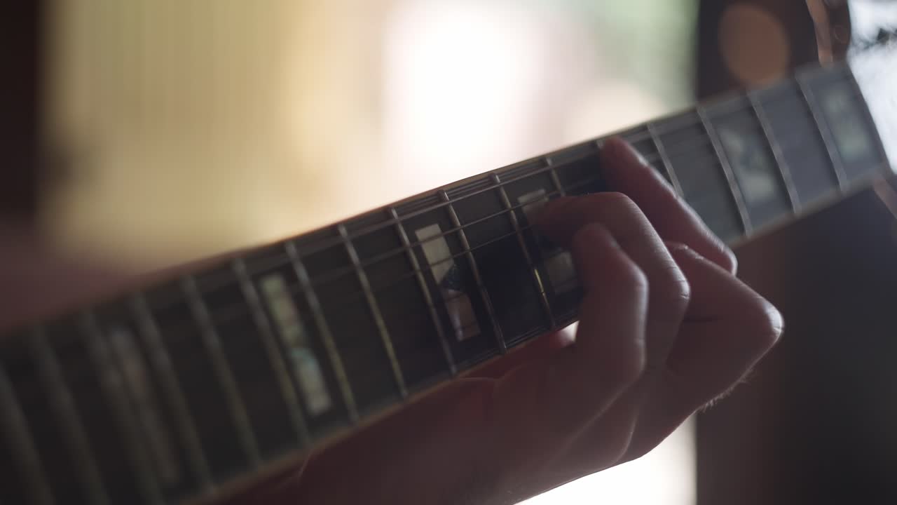 Close up view of a Man's hand playing an electric guitar in a home studio during sunset hours