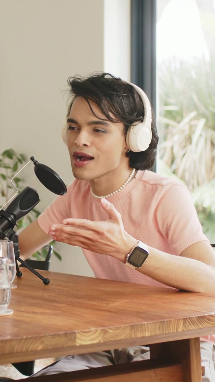 Video verticale: Inclinato verso il microfono, un creatore parla nel microfono in uno studio casalingo, registrando un podcast.
