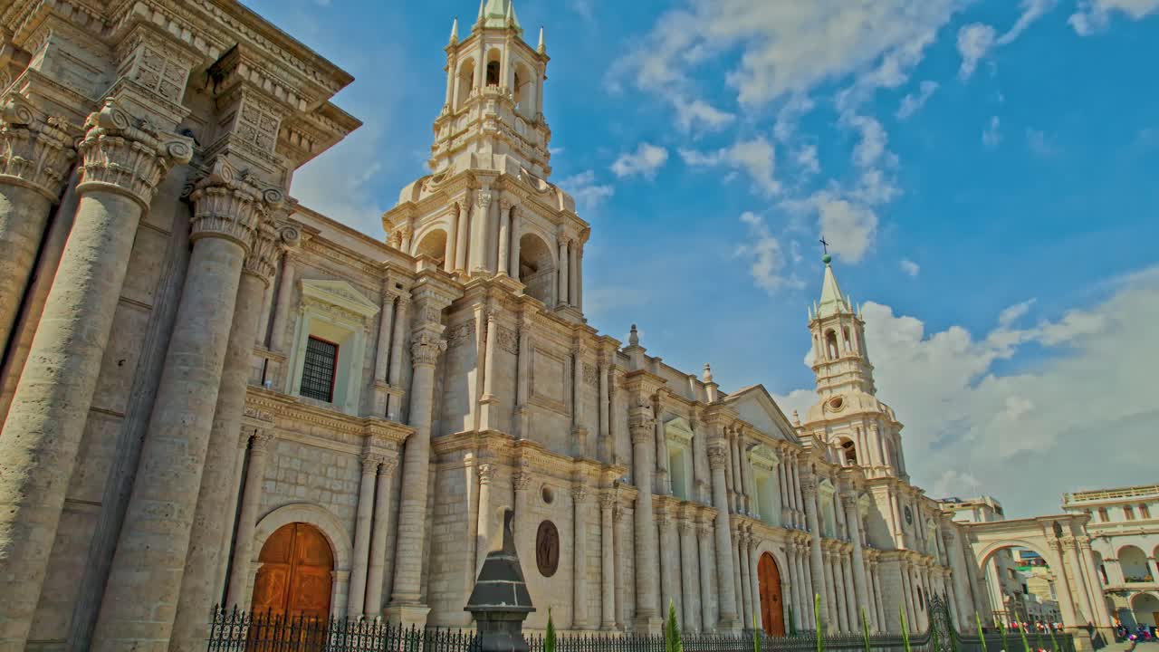 아레키파 대성당의 드론 판, 왼쪽 포털에서 시작하여 오른쪽 탑과 전체 대성당을 드러내고, 산란한 구름과 함께  ⁇ 은 날에 지역 나무로 끝납니다.