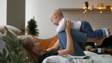 mom plays with baby in white tank top lying on the bed, baby flying and laughing. time lapse of playing together mother and child. flight simulation