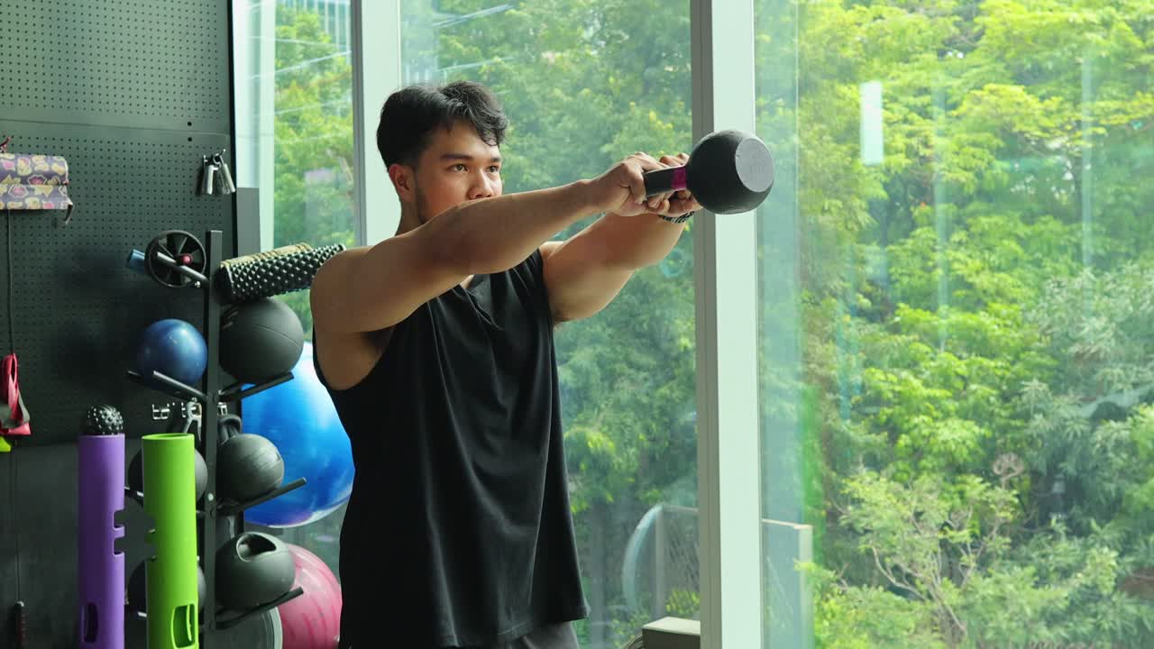 Athletic man performs kettlebell swing in sunlit gym with modern equipment and large windows