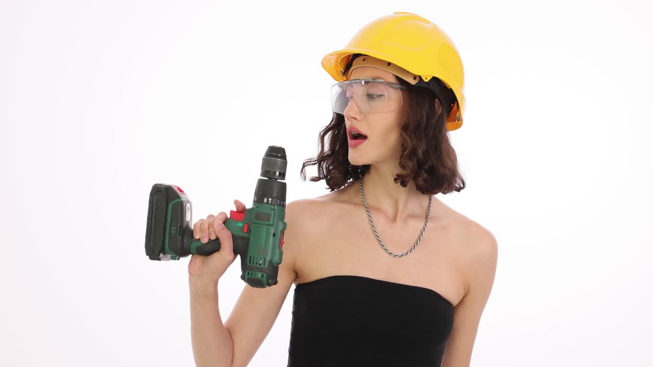 A woman in a hard hat and safety glasses holding a power drill