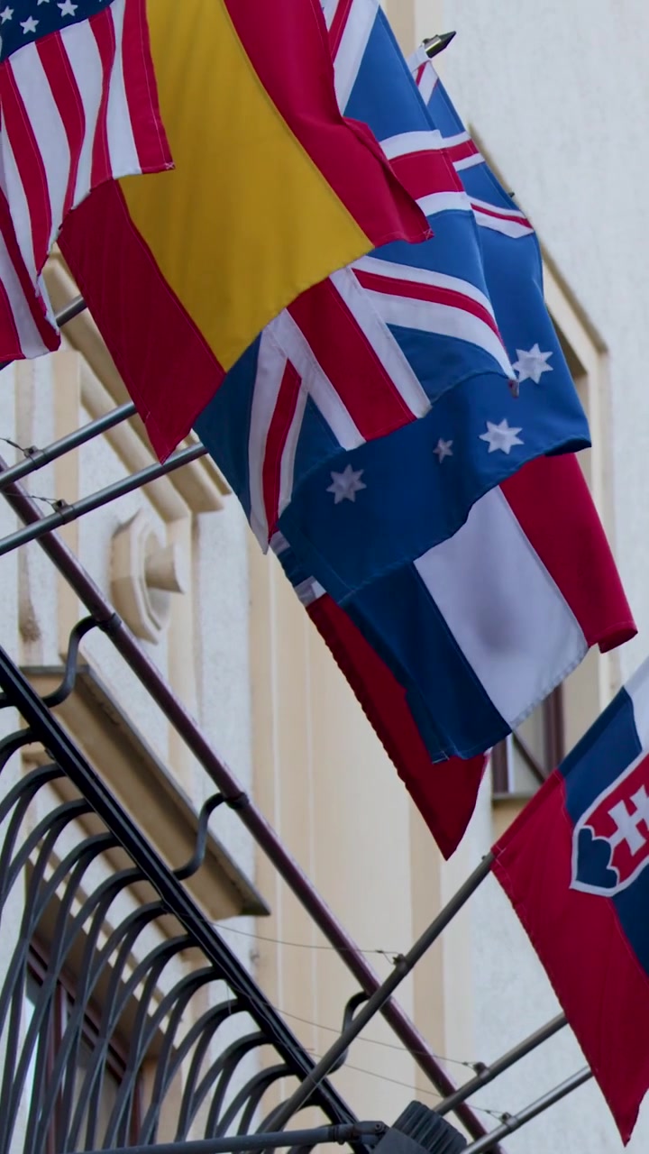 Multiple national flags wave from an ornate historic building facade in a vertical composition.