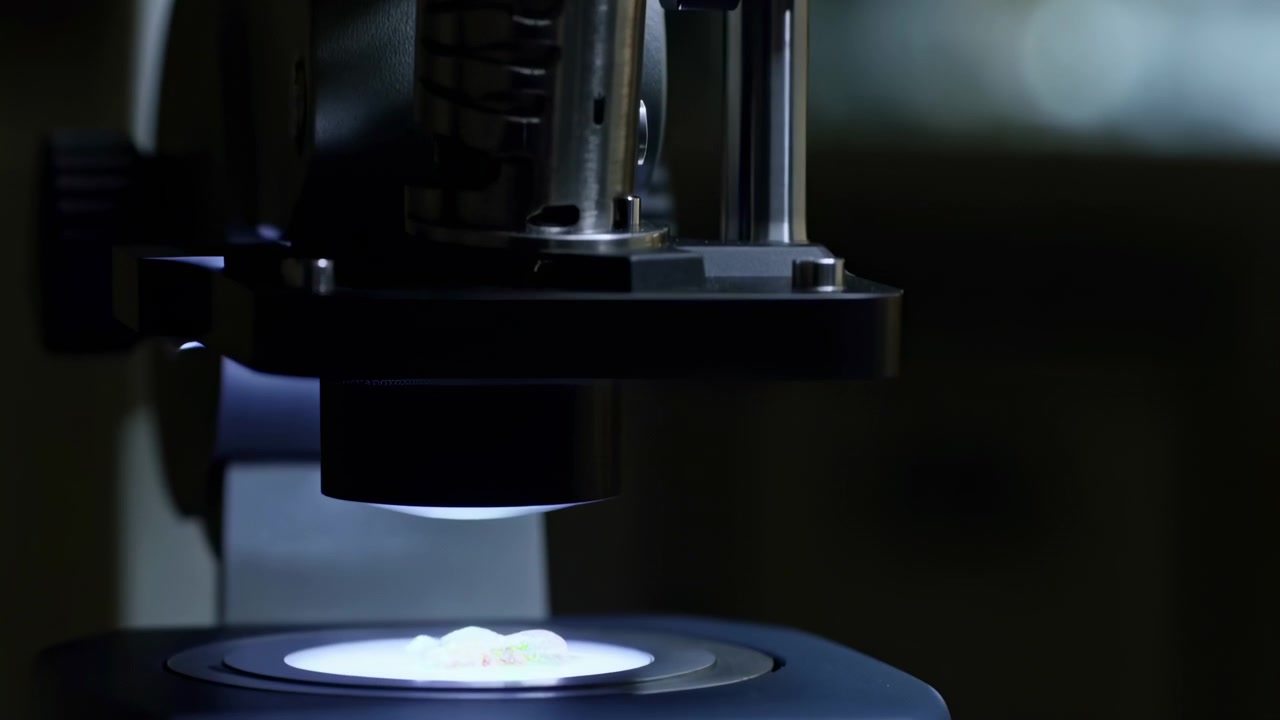 Close up motion view of binocular microscope with glowing lens reflections, matte black housing, aligned eyepieces and focused stage surfaces as examination details gradually reveal support column