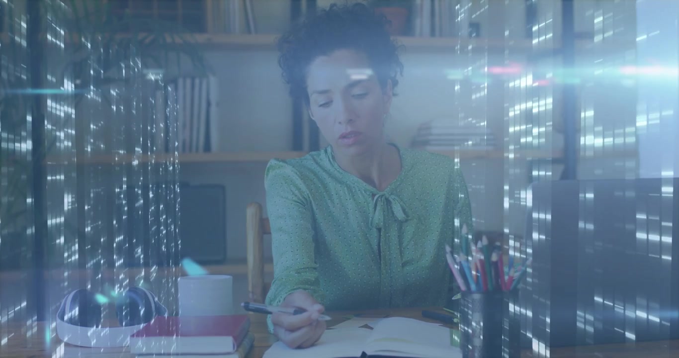 Woman sitting reaching for pen and writing notes for study while vertical lights overlaying journal