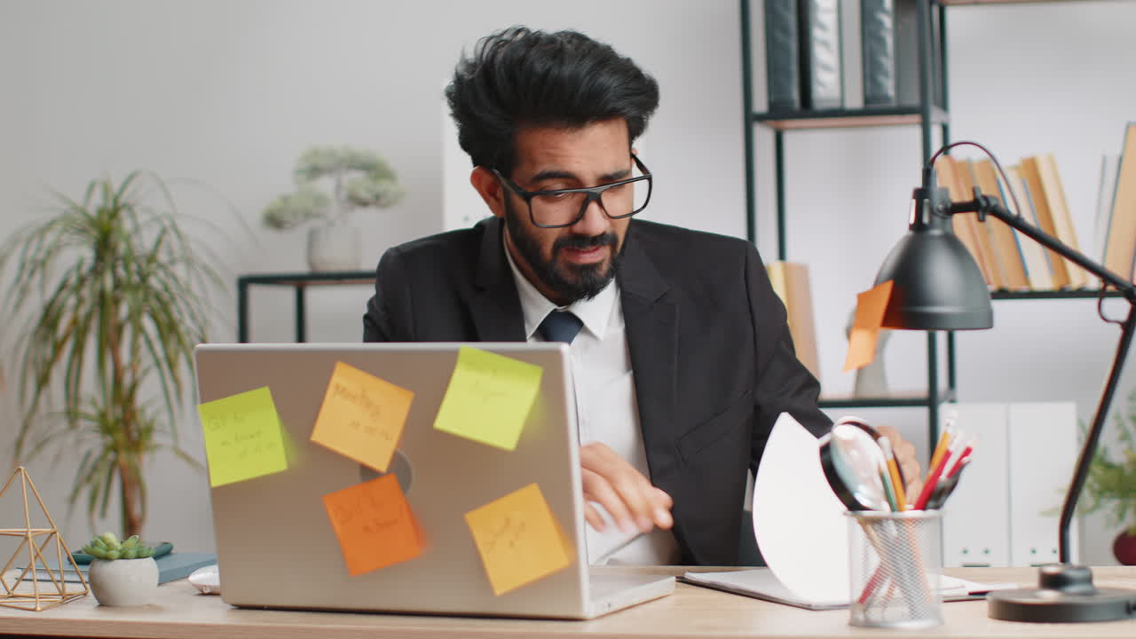 Tired sad exhausted businessman working on laptop at office with many sticker tasks panic attack