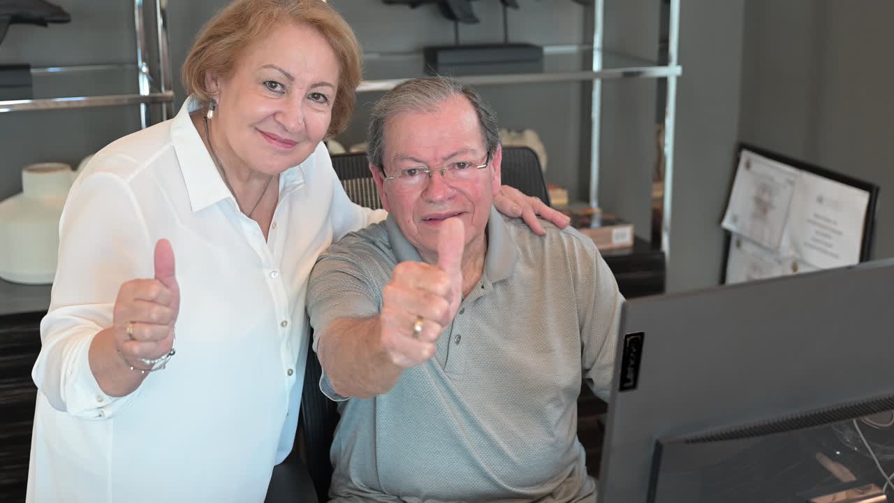 una pareja jubilada se sienta detrás de una computadora en la oficina y da un pulgar hacia arriba en su reciente decisión de compra