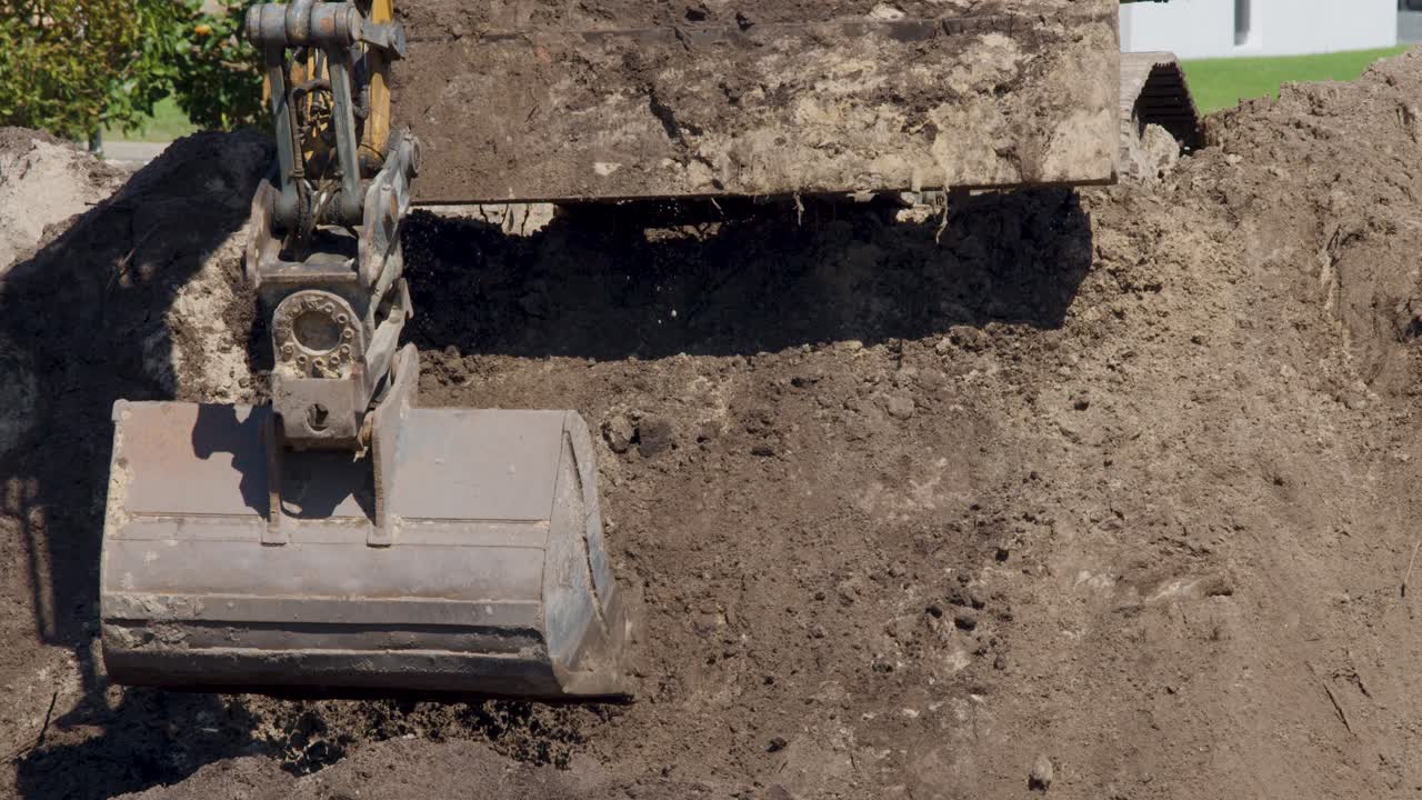 Excavator bucket scoops and lifts soil in bright daylight at an outdoor construction site