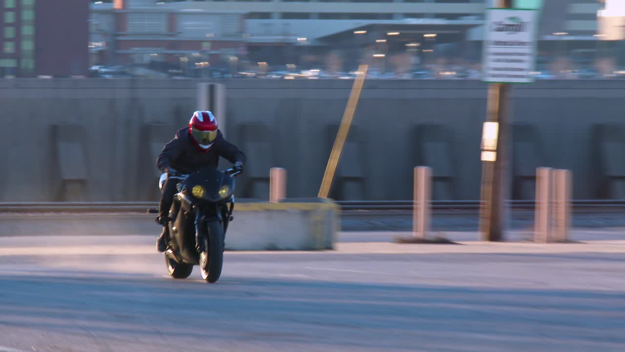 A rider performs stunts on a motorcycle in a parking lot 3