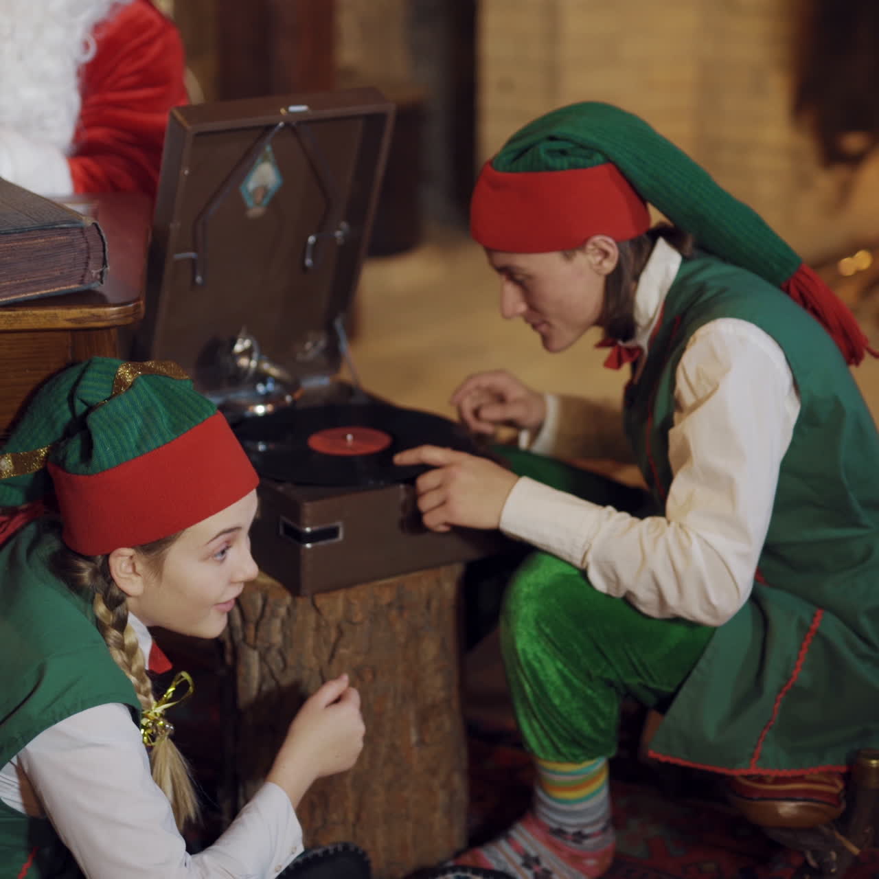 Two elves with old disk in Santa's residence. Happy elves in green costumes putting big disk into old tape recorder.