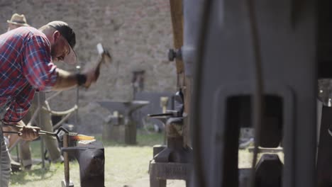 a blacksmith hammers hot iron on an anvil in an outdoor workshop.