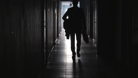 rear view of businessman walking along dark hallway