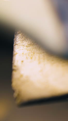 cu shot: skilled jeweler polishes gold rod with rasp and cleans equipped workplace in light workshop close view