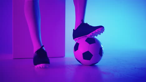 close-up of the foot of a professional black football player standing on the ball in slow motion in the blue-red neon light of the studio. brazilian football player foot on the ball to pose