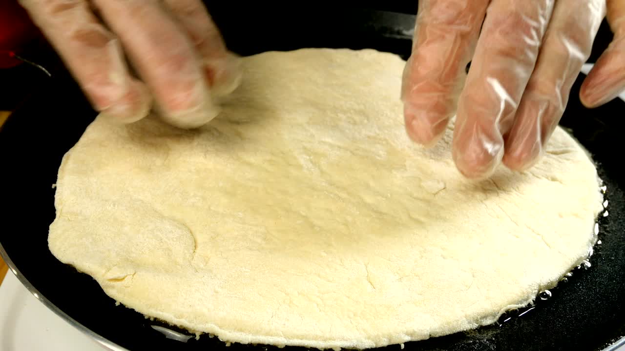 el chef pone en la sartén caliente con aceite de oliva, pan plano de bruja hecho de masa sin levadura.