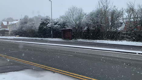 a small lonely bus stop on the side of a busy road covered in snow while it is snowing at christmas time