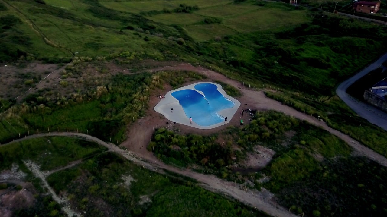 Luftfoto af et landligt landskab med frodige grønne marker, en snoet sti og en blå dam. Scenen indfanger landskabets naturlige skønhed, ro og vidtstrakte udsigter