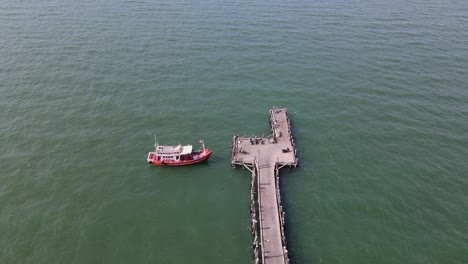 Imágenes-Aéreas-Estables-Del-Final-Del-Muelle-De-Pesca-De-Pattaya-Que-Revelan-Un-Barco-De-Pesca-Atracado-Y-Algunas-Motocicletas-Mientras-Un-Pájaro-Vuela,-Pattaya,-Tailandia