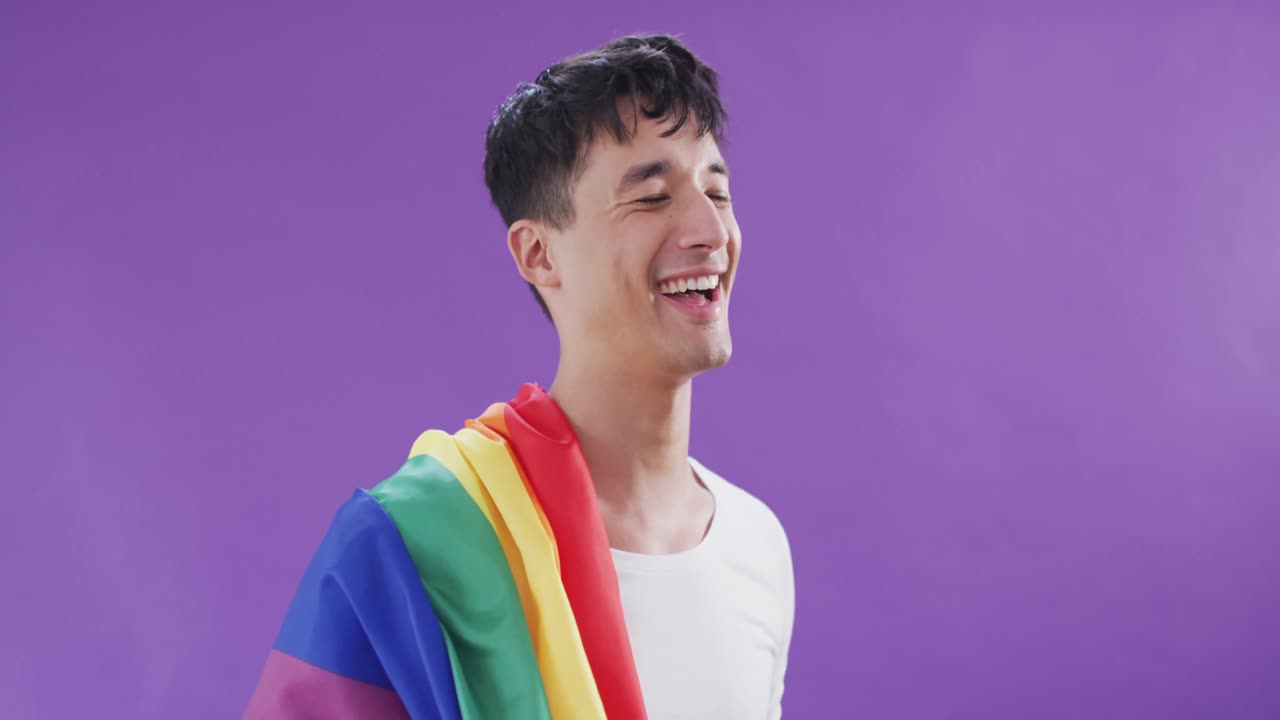 Happy biracial man holding lgbt flag on shoulder and smiling