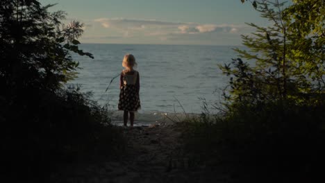 silhouette shot of little girl running down path to the beach and looking out at the water