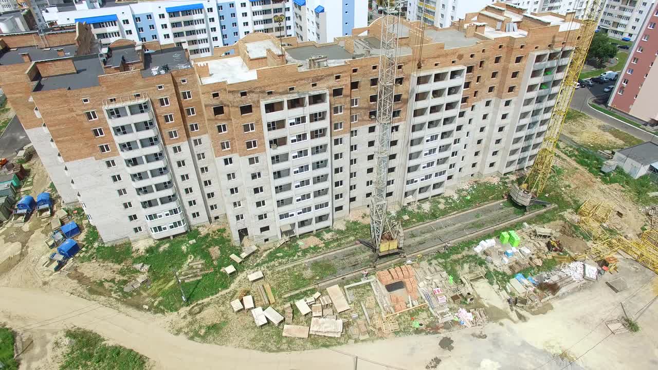 Building construction of the modern residential complex with two cranes near the multy-storey in a sunny day. New house is building in a city. Motion top down.