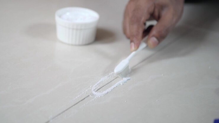 Person Scrubbing Tile Grout with Toothbrush and Cleaning Powder