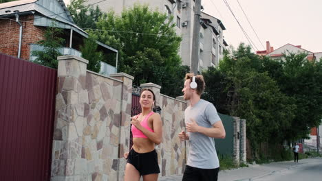 bella corredora con airpods y joven deportivo con auriculares hablando y corriendo juntos en la ciudad