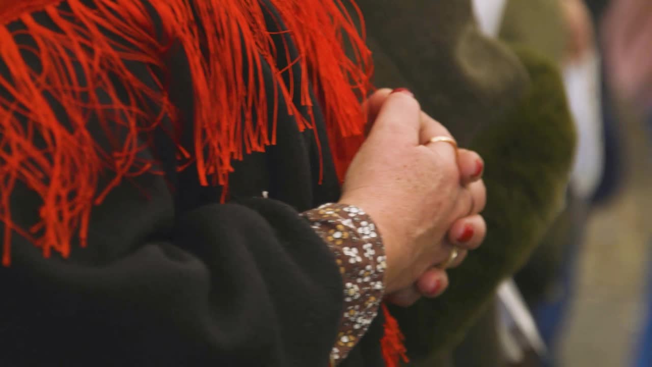 Woman with red nails clasping hands, red shawl, bracelets. Detail shot