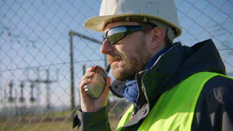 male engineer listening over the walkie talkie while nodding his head at the electric substation, handheld closeup