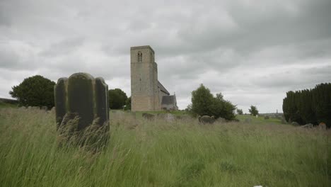 viento que sopla a través de un cementerio cubierto que muestra una antigua iglesia medieval en el fondo y un espectacular cielo nublado