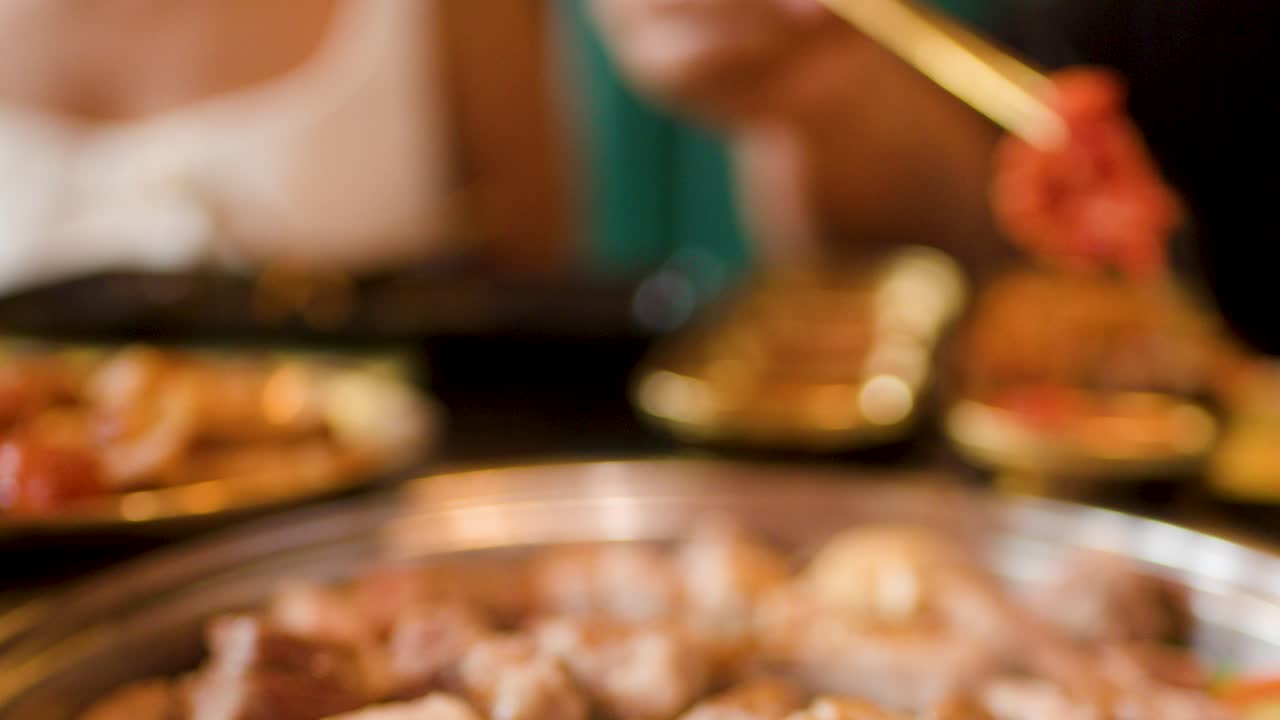 Person uses tongs to grill pork and chicken on a smoky tabletop Asian barbecue grill