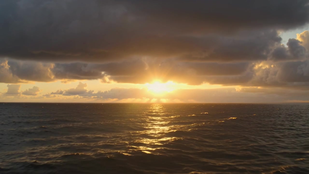 Shining sun nearing horizon casting sun gleam across ocean waves under horizon cloud, bank glowing