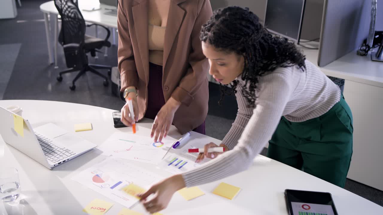 After man pointing at chart, coworkers writing, stamping sticky notes on table for planning targets