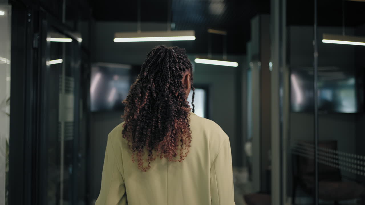 la cámara sigue la espalda de una mujer negra de negocios por el pasillo
