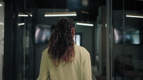 The camera follows the back of a business black woman down the corridor